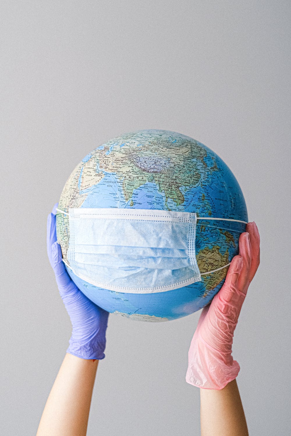 world globe with face mask held by gloved hands